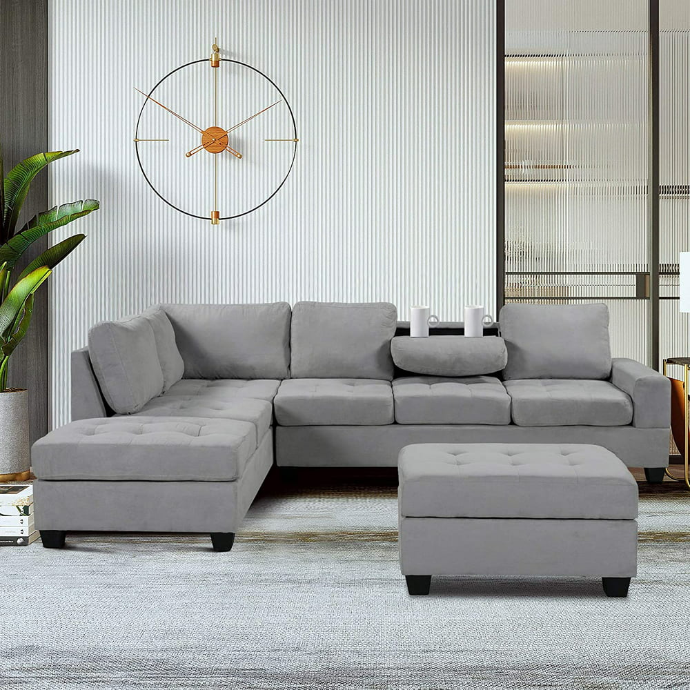 A modern living room features a plush gray sectional sofa with an ottoman. The sectional has a chaise lounge on the left side. A stylish wall clock and tall green plant accent the room. Neutral tones and soft lighting create a cozy atmosphere.