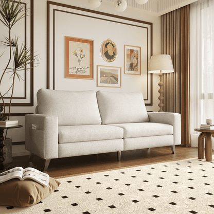 A cozy living room showcasing the YODOLLA 79" Sectional Sofa in beige, accompanied by a textured rug with a dotted pattern, framed art adorning a white paneled wall, a potted plant for greenery, and a wooden side table topped with a lamp. Sunlight flows through sheer curtains.