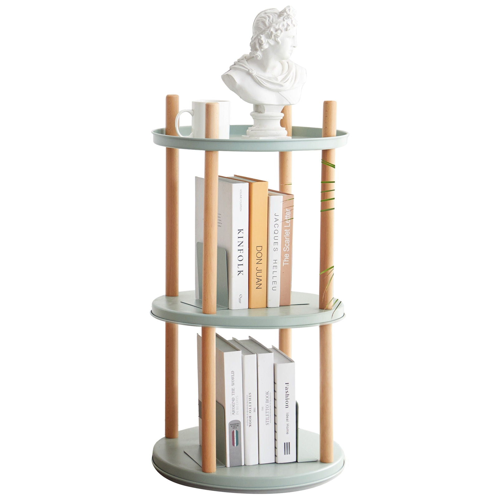 A compact, multifunctional 360° rotating bookshelf with light green shelves and wooden supports holds a white statue bust, a white mug, and several books both upright and stacked flat.