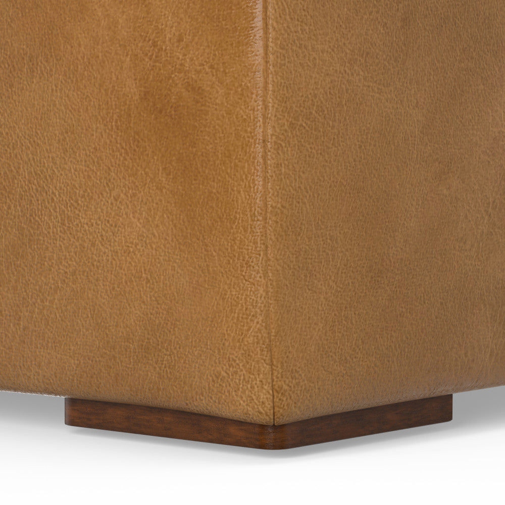 Close-up of a light brown leather sofa corner showing the textured surface and wooden base. The material has a slightly distressed look, and the wooden base appears polished and dark in contrast with the leather.