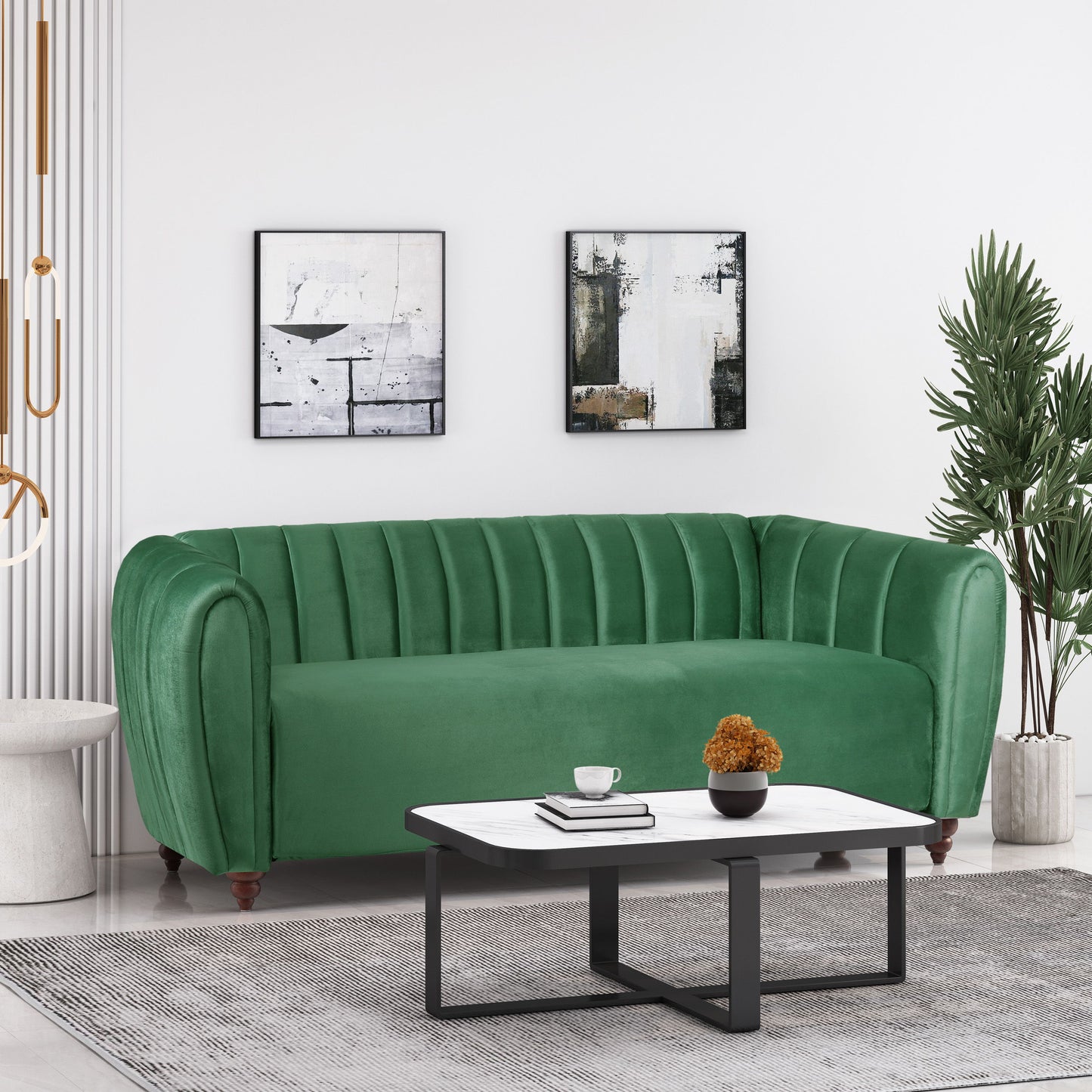 A modern living room showcases a plush 3 Seater Sofa in green with glam design, two abstract wall paintings, and a sleek black and white coffee table adorned with a plant. A tall green plant in the corner completes the minimalist decor.