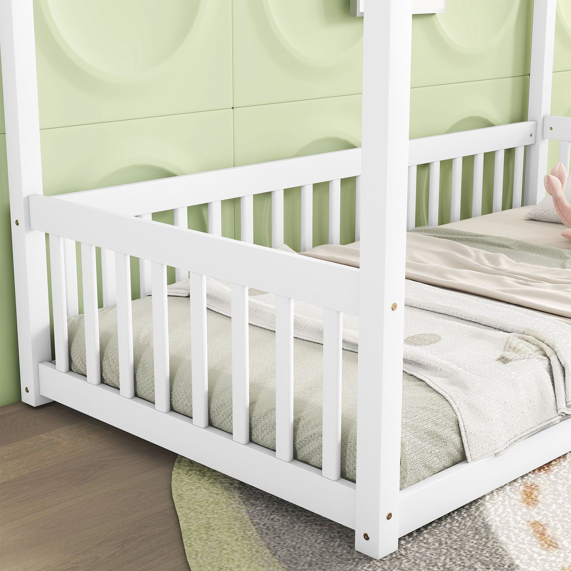 A white Canopy Frame Floor Bed With Fence and guardrails sits against a light green textured wall, featuring a soft green blanket and a beige stuffed animal. Light brown flooring includes a partially visible round, patterned rug.