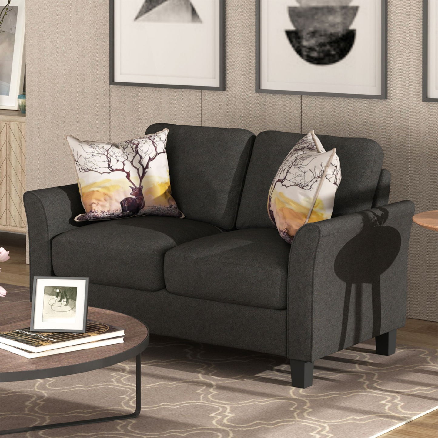 A dark gray Living Room Furniture Love Seat Sofa Double Seat Sofa Loveseat Chair with two tree-design pillows is in a living room. Framed abstract art hangs behind it. Nearby, a round coffee table with books and a picture frame sits on a patterned rug.