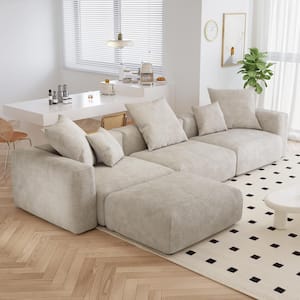 A modern living room features a spacious black square arm 4-piece L-shaped corduroy polyester sectional sofa, accented with scattered cushions, resting on a light herringbone wood floor. In the background, a white dining table accompanied by wooden chairs is situated beside a window with blinds. The scene is completed with a potted plant and minimalist decor.