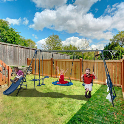 Three children enjoy the Interesting Six Function Swingset in a backyard; one slides, another raises arms on the 31.5" net swing, and the third swings joyfully. A wooden fence borders the yard under a bright, cloudy sky.