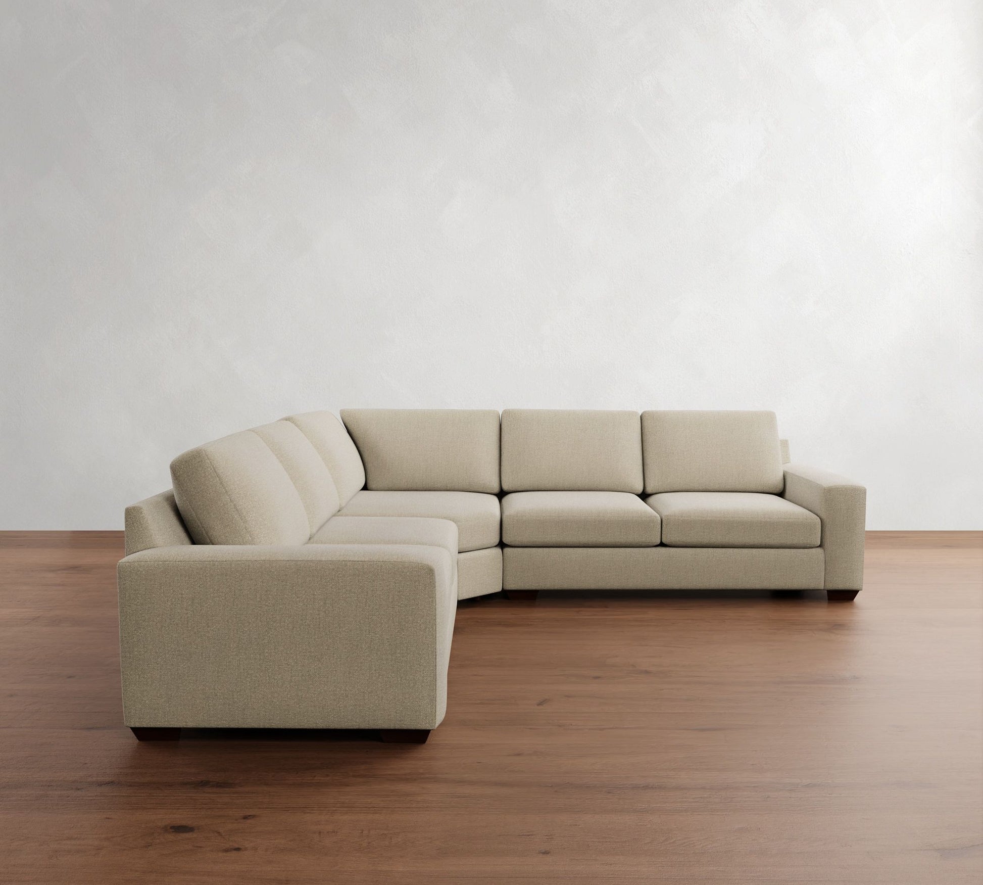 A light gray wall and wooden floor accentuate the modern and minimalist style of the Big Sur Square Arm Upholstered 3-Piece L-Shaped Wedge Sectional, which sits prominently in the otherwise empty room.