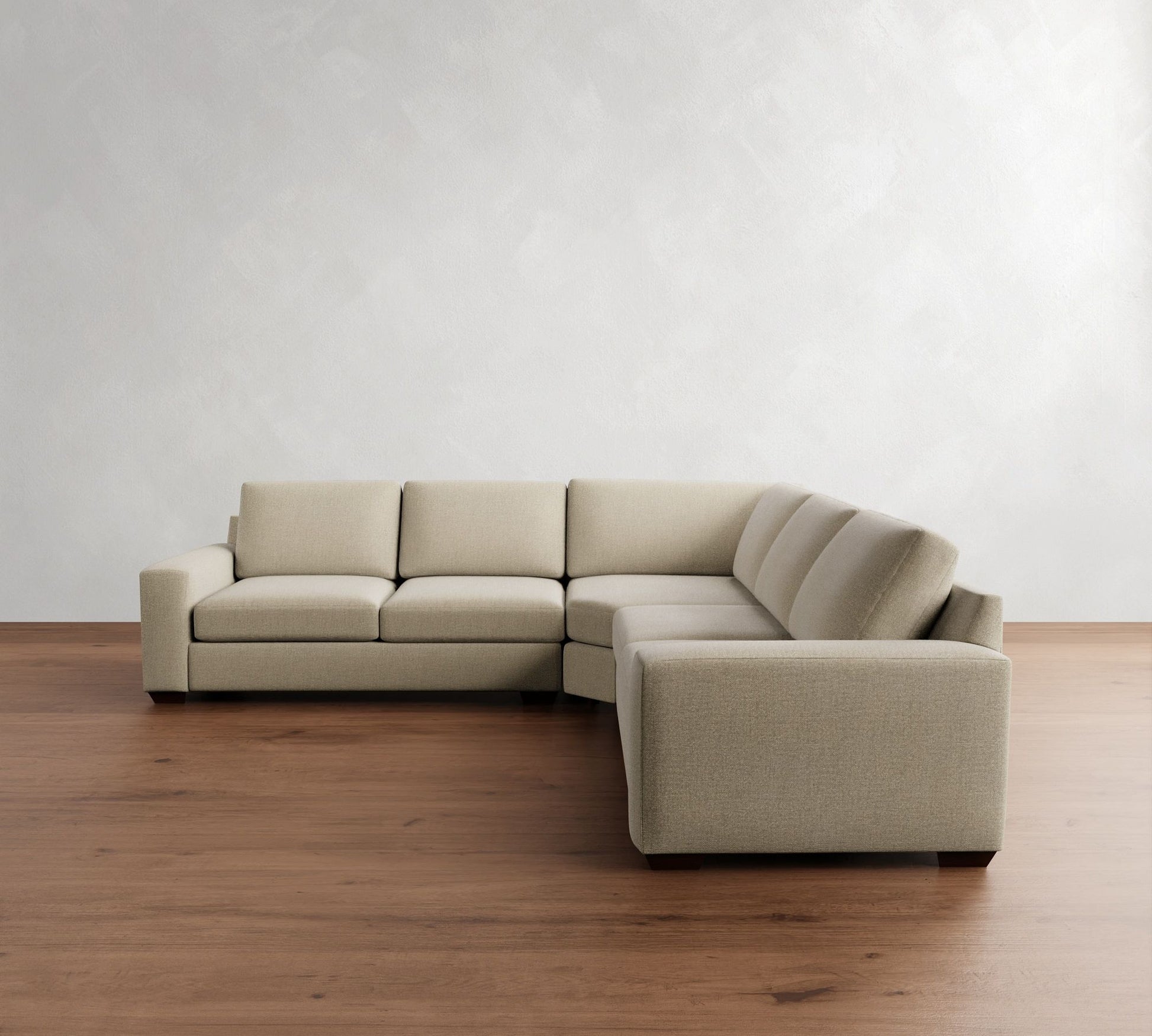 The Big Sur Square Arm Upholstered 3-Piece L-Shaped Wedge Sectional, in beige, is positioned on a wooden floor against a light gray textured wall. This modern and minimalistic sofa provides plenty of seating.