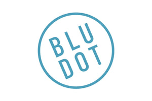 A simple logo featuring the words "BLU DOT" in uppercase blue letters, set at an angle within a blue circle against a white background.