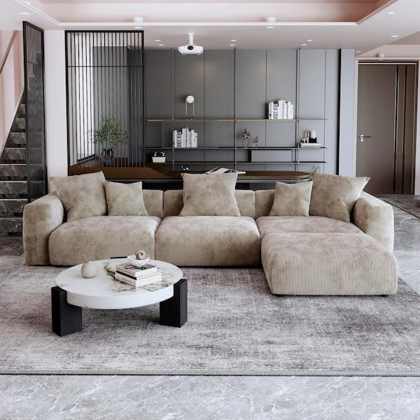 A modern living room with a 142-inch square arm 4-piece L-shaped corduroy polyester sectional sofa in black and a round marble coffee table. The room features gray patterned flooring, a staircase, bookshelves, and minimalist decor against a backdrop of dark vertical panels and built-in shelves.