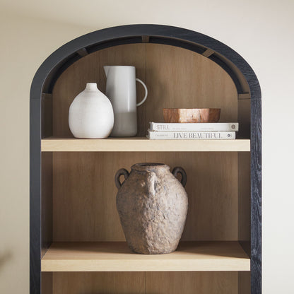 The Modern 5 Shelf Open Arched Bookshelf features a black frame and elegantly displays a white vase, gray pitcher, books, and a small wooden bowl on the top shelf. A large rustic clay jug adorns the middle shelf.