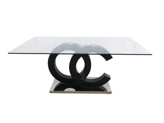 The Aston Dining Table features a sleek and contemporary design with a modern glass rectangular top, supported by two interlocking black C-shaped metal structures on a square stone base.