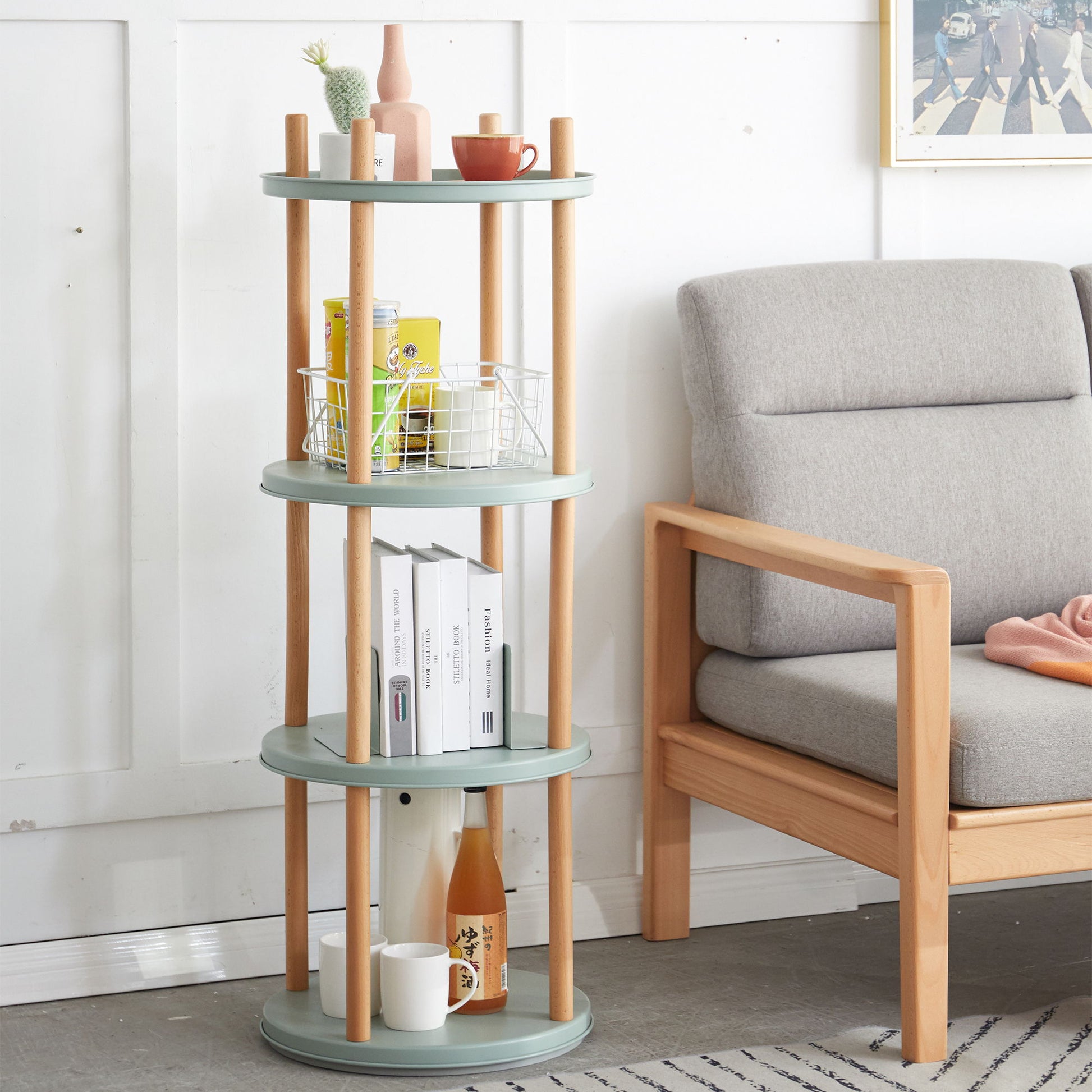 A round, multi-tiered teal Storage Shelf with 360° rotation holds decor items beside a light gray cushioned wooden armchair in a modern living room.