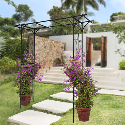 A scene showcases a black Metal Garden Arch Climbing Plants Support, adorned with two pots of vibrant purple flowers. Behind it, white stone steps lead to a modern house with open wooden doors, surrounded by lush greenery.