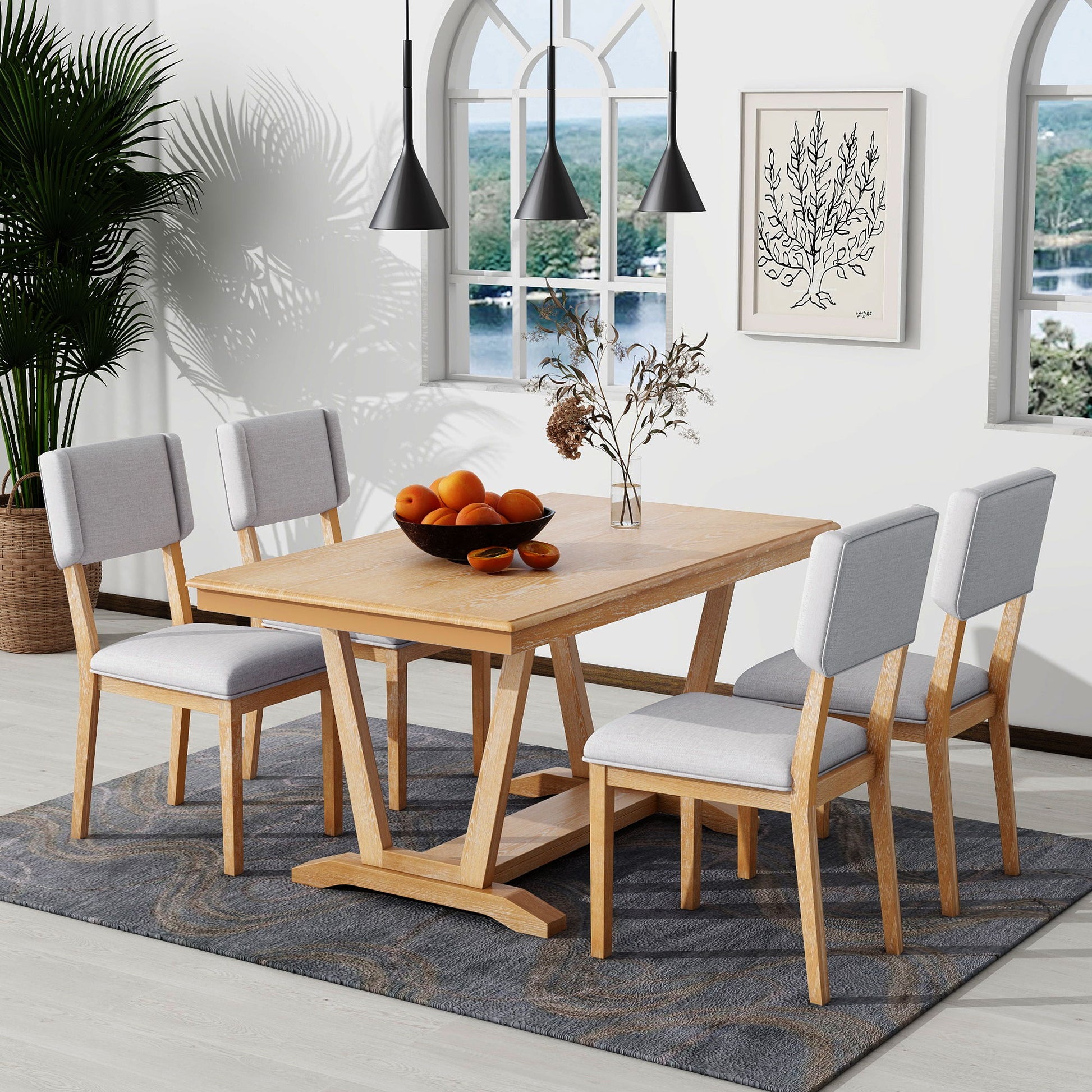 A dining room featuring the Topmax 5 Piece Rustic Dining Table Set with a rectangular wooden table and four gray upholstered chairs on a patterned rug. A bowl of oranges and dried flowers adorn the table, with three pendant lights above, a nature view window, and plant artwork on the wall.