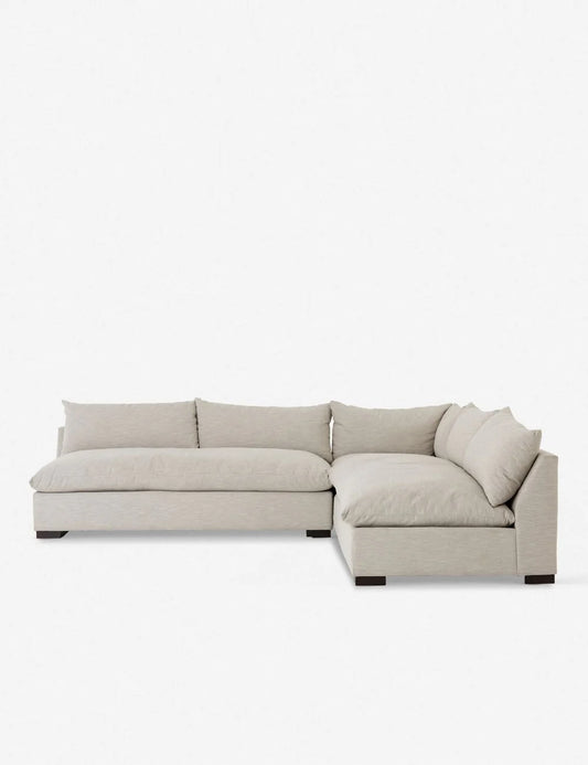 The Decima Sectional Sofa, an L-shaped piece in light gray, stands against a plain white backdrop. It features low backrests and thick cushions that contribute to its minimalist, modern design and soft, inviting appearance.