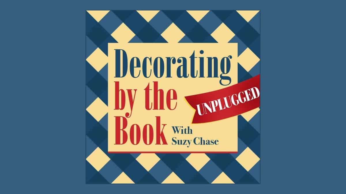 A square graphic with a checkered blue and yellow background. Text reads "Decorating by the Book" in red and "With Suzy Chase" in black. A red ribbon across the right side says "UNPLUGGED" in white.