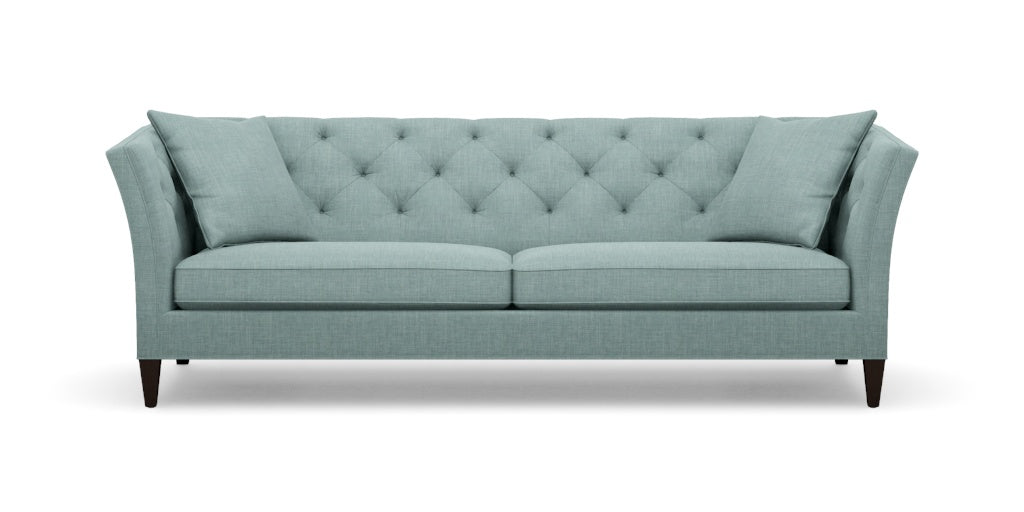 The Shelton 98" Sofa is a stylish piece, featuring a tufted backrest and two seat cushions in a chic teal color. It boasts flared armrests and rests on dark wooden legs, seamlessly combining contemporary design with comfort.