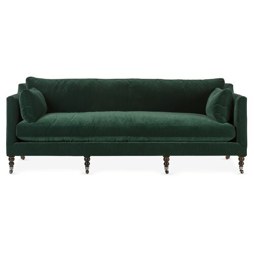 Introducing the Margot Velvet Sofa: a dark green masterpiece with round cushions at each end, supported by elegant wooden legs and featuring a classic design. It boasts a straight back and sleek armrests for added sophistication.