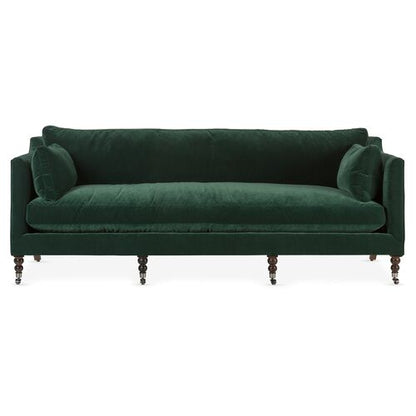 Introducing the Margot Velvet Sofa: a dark green masterpiece with round cushions at each end, supported by elegant wooden legs and featuring a classic design. It boasts a straight back and sleek armrests for added sophistication.