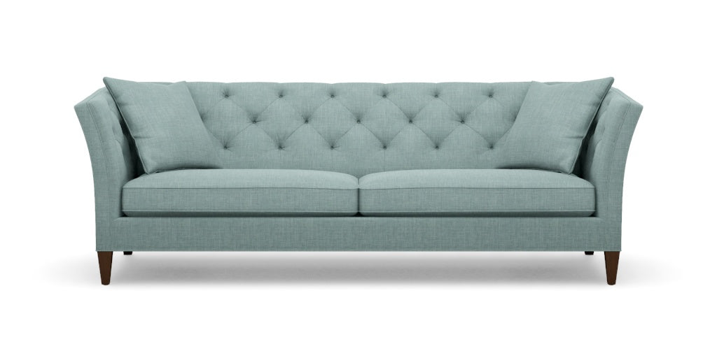 The Shelton 98" Sofa boasts a light teal color with tufted upholstery, featuring an angled backrest and cushions. Its wooden legs and contemporary design offer a stylish and comfortable two-seat seating option.