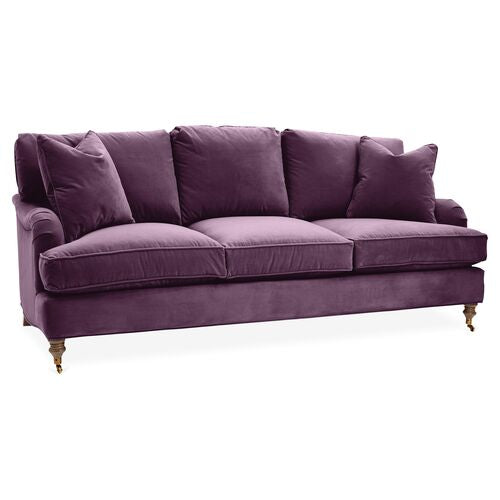 The Brooke 6-Seat Sofa is a chic addition to any living room, offering purple velvet upholstery with three seat cushions and four plush back pillows. It features elegantly rounded armrests and rests on wooden legs equipped with small wheels, blending a modern touch with timeless elegance.