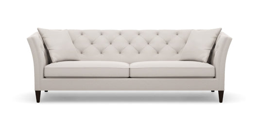 Introducing the Shelton 98" Sofa: a cream-colored masterpiece with a contemporary flair, featuring a tufted backrest and two perfectly matching throw pillows. The design boasts sleek, slightly flared arms complemented by elegant wooden legs, all showcased against a plain white backdrop.