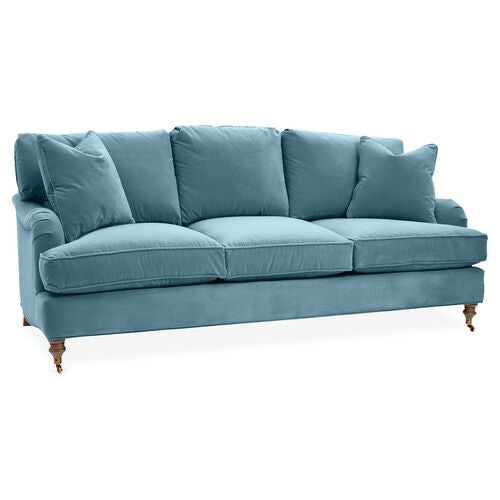 Introducing the Brooke 6-Seat Sofa: a light blue seating solution featuring plush cushions and rolled armrests. This sofa is designed with three seat cushions and is supported by four wooden legs, each equipped with small wheels for easy mobility.