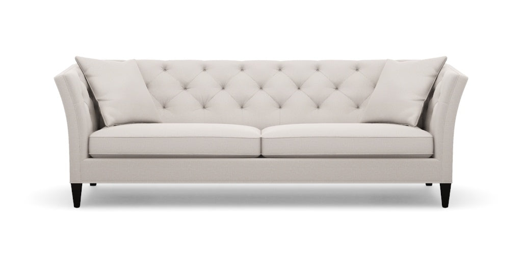 The Shelton 98" Sofa features a sleek and modern design with a beige tufted finish, two seat cushions, and angled arms. It is supported by dark wooden legs and comes with two matching throw pillows on each end, all set against a plain white background.