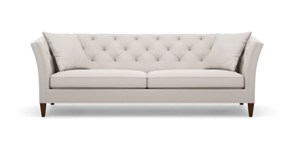 The Shelton 98" Sofa is a light gray tufted sofa with two cushions, showcasing a modern design with angled armrests and dark wooden legs, set against a white background.