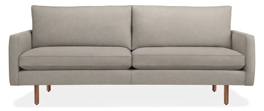 The 86" Jasper Sofa is a modern piece with a light gray finish, featuring clean lines and a minimalist design. It includes two large seat cushions and two back cushions, all supported by slim wooden legs, exuding contemporary elegance.