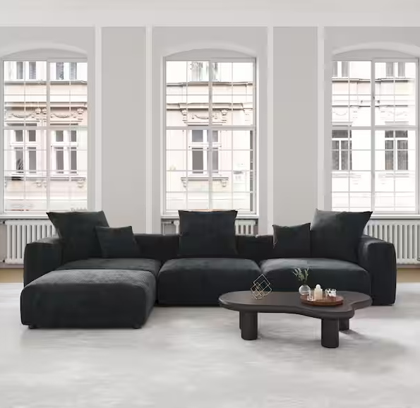 A spacious living room showcases the 142 in. Square Arm 4-Piece L-Shaped Corduroy Polyester Modern Sectional Sofa in black, elegantly arranged in front of six tall, arched windows. The room also includes a dark wooden coffee table and white walls, cultivating a minimalist and modern atmosphere.