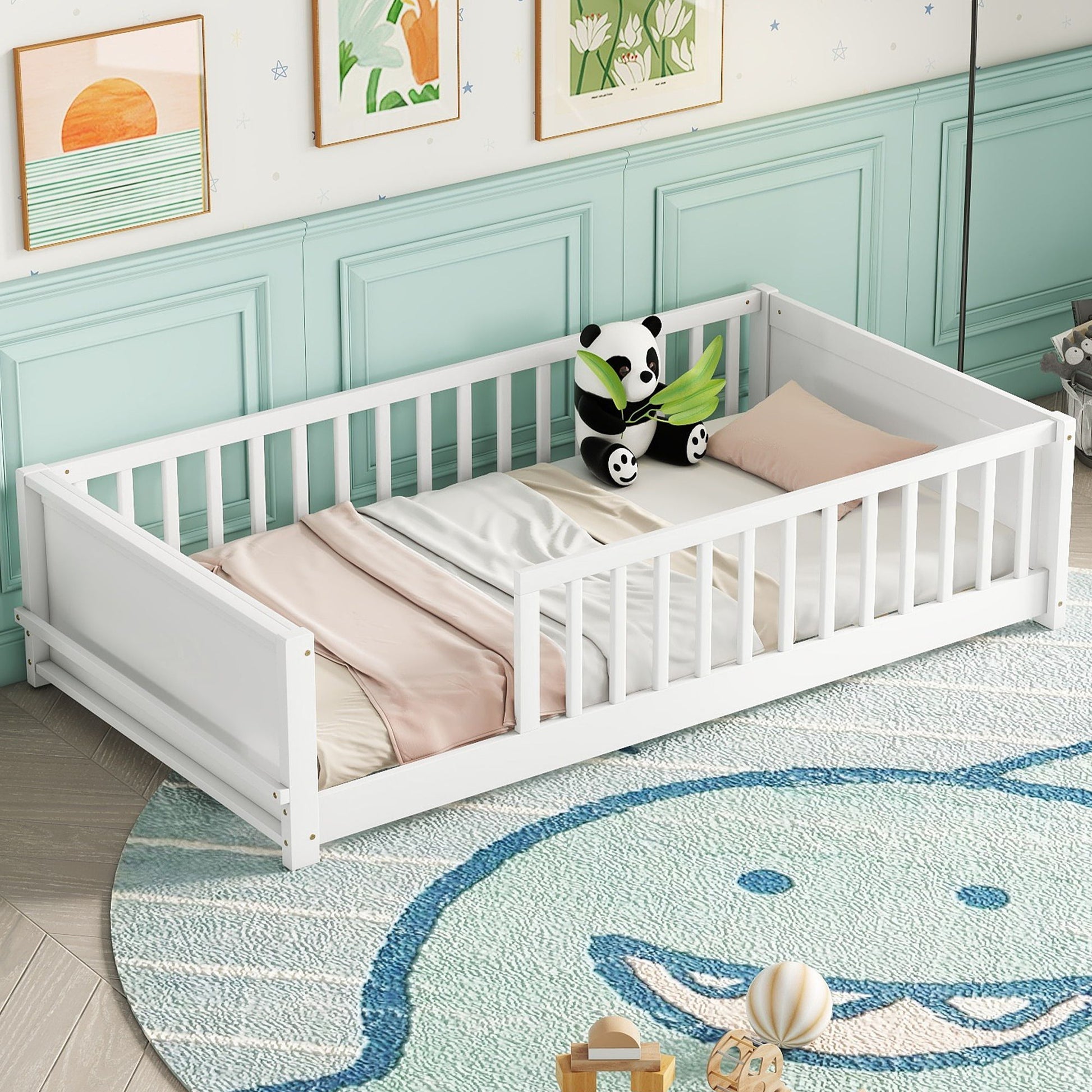 A toddler bed named Floor Platform Bed With Built-In Book Storage Rack, with white frames and light pink bedding, is set in a room with green paneling. A plush panda toy rests on the bed. The floor has a rug featuring a smiling whale design, and artwork decorates the wall above it.