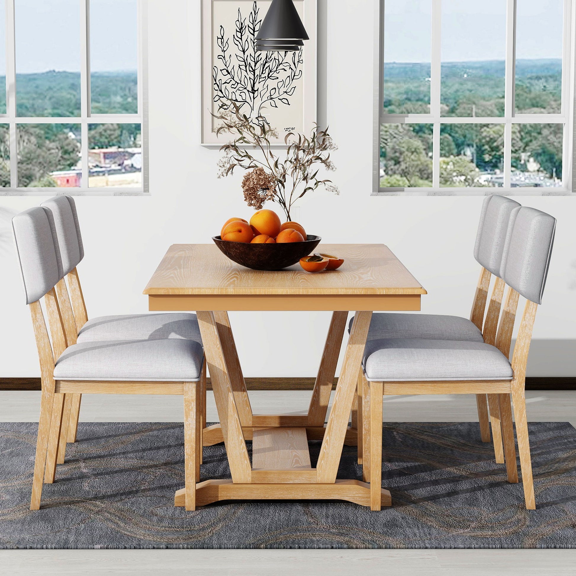 The Topmax 5 Piece Rustic Dining Table Set, featuring a trestle base and four upholstered chairs, is adorned with a decorative bowl of oranges and dry branches. It sits on a patterned rug in a room with large windows overlooking greenery and buildings.