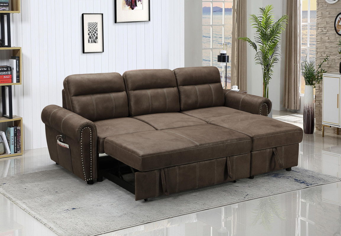 In the middle of a modern living room, the Hugo Reversible Sleeper Sectional Sofa Chaise With USB Charger in brown is set up. It features plush cushions and a side pocket. The room boasts white panel walls, minimalist decor, indoor plants, and a large window with a view.