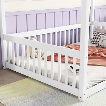 A cozy Canopy Frame Floor Bed With Fence, Guardrails rests against a light purple paneled wall. It features a pink blanket, plaid pillows, a teddy bear, and a small book. A soft, multicolored rug adorns the wooden floor.