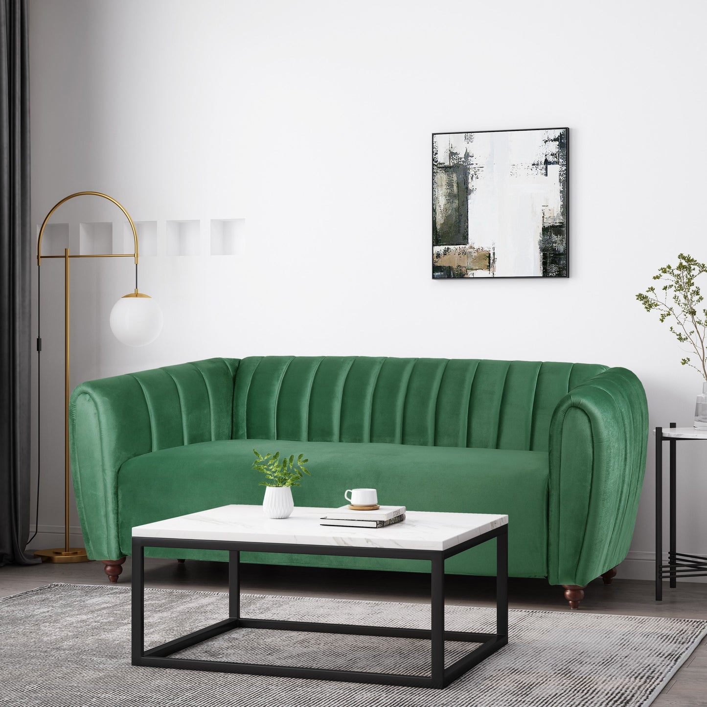 A modern living room with a green velvet 3 Seater Sofa Modern Glam Design featuring vertical tufting, a rectangular white and black coffee table, and a tall gold floor lamp with a spherical white shade. A minimalist abstract painting hangs on the white wall.