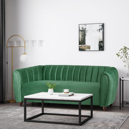 A modern living room with a green velvet 3 Seater Sofa Modern Glam Design featuring vertical tufting, a rectangular white and black coffee table, and a tall gold floor lamp with a spherical white shade. A minimalist abstract painting hangs on the white wall.