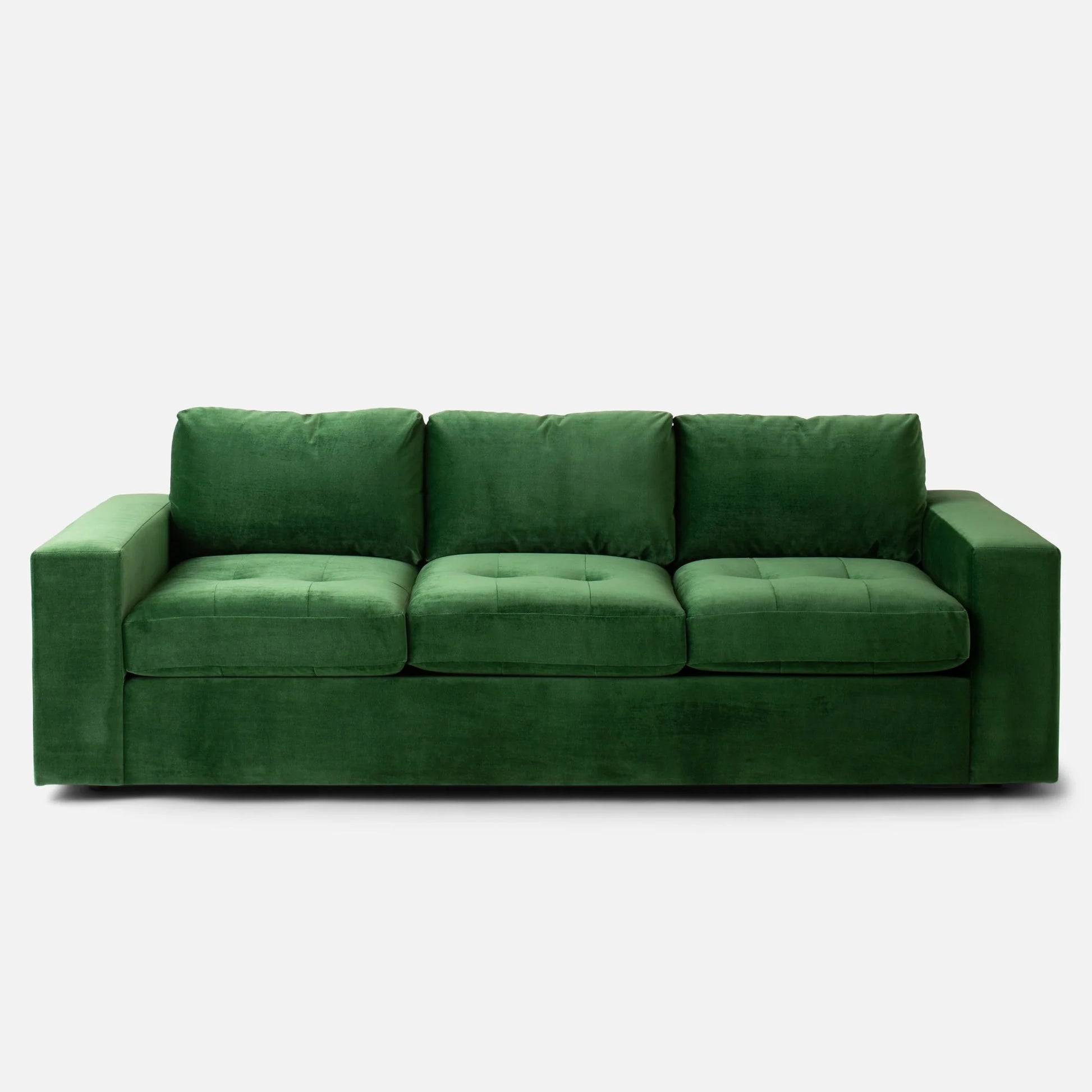 Marc Tufted Sofa in a rich green velvet, featuring three large cushioned seats and wide armrests. The sofa showcases a simple, modern design and is set against a plain white background.