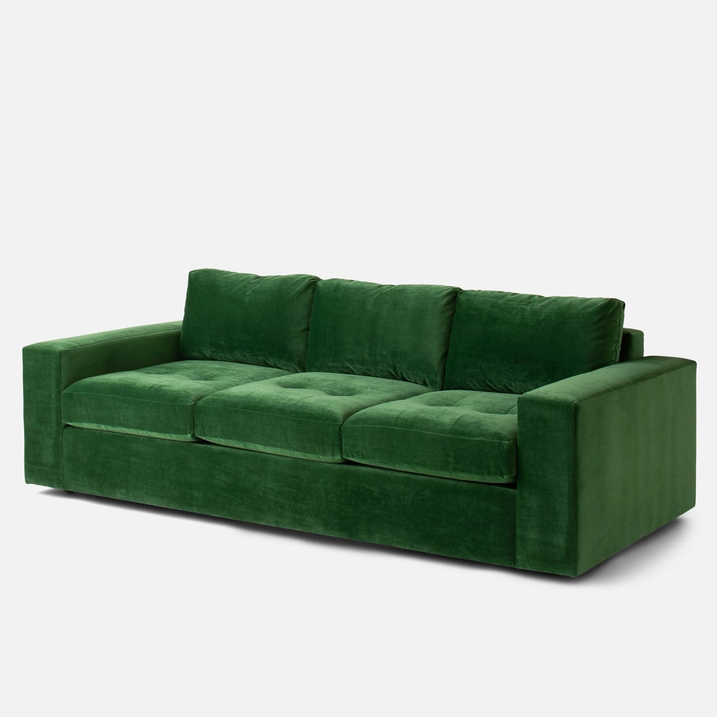 The Marc Tufted Sofa, a plush piece made from green velvet, features three large cushions and wide armrests, set against a plain white background.