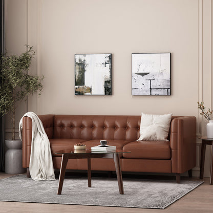 A cozy living room showcases the Comfy 3 Seat Sofa With Tufted Back in brown leather, adorned with a beige pillow and white throw. A wooden coffee table on a gray rug holds a small plant, book, and mug. Two abstract paintings hang on the light beige wall.