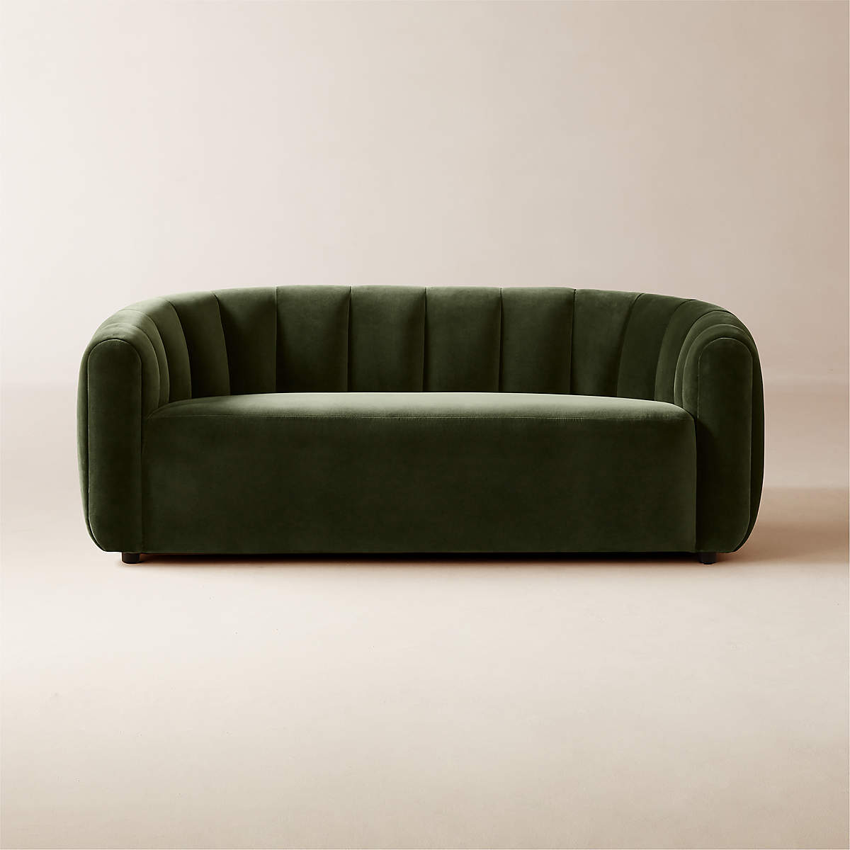 The Fitz 72.5" Channeled Green Velvet Loveseat, featuring a rich green hue and distinctive vertical tufting, rests on a light beige backdrop. Its modern and plush design exudes a luxurious and welcoming feel.