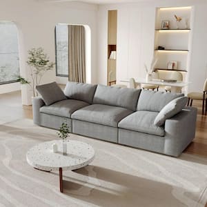 A contemporary living room featuring a spacious 142-inch square arm L-shaped sectional sofa in black corduroy polyester, accompanied by a round white coffee table and minimalist decor. The room showcases white walls with a small potted plant next to the sofa. Natural light floods the space through the windows, and a dining area can be seen in the background.