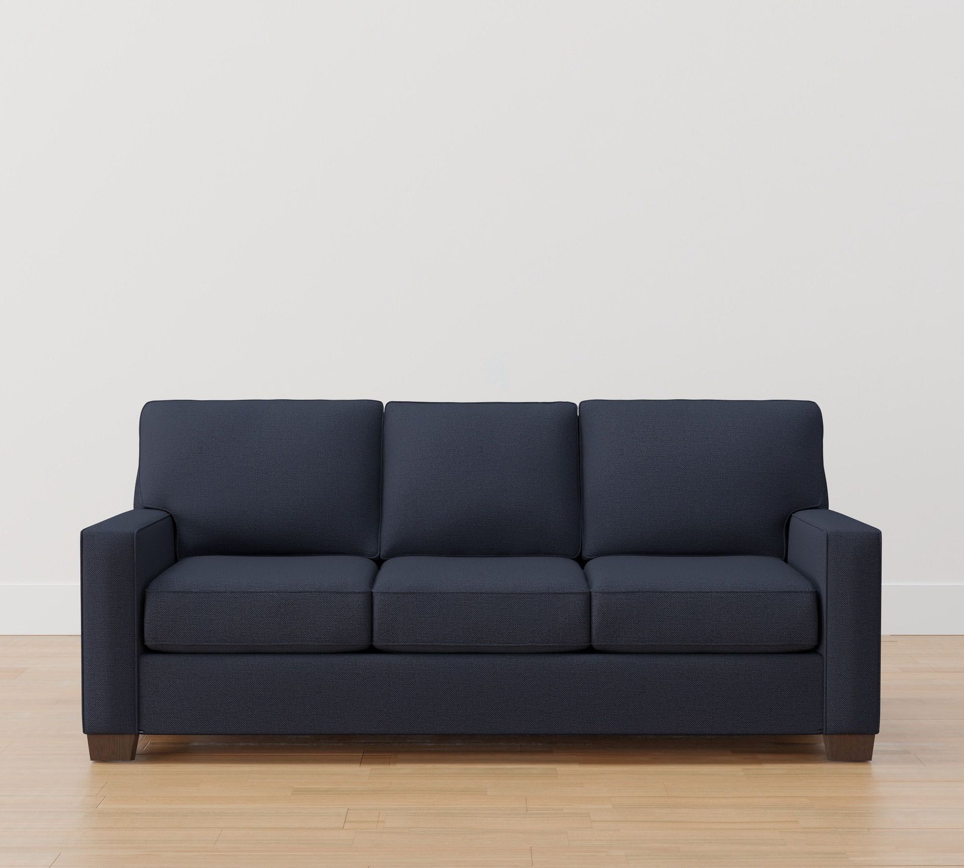 A Buchanan Square Arm Sleeper Sofa in dark blue, featuring a minimalist design and straight arms, is placed on a light wooden floor against a white wall.