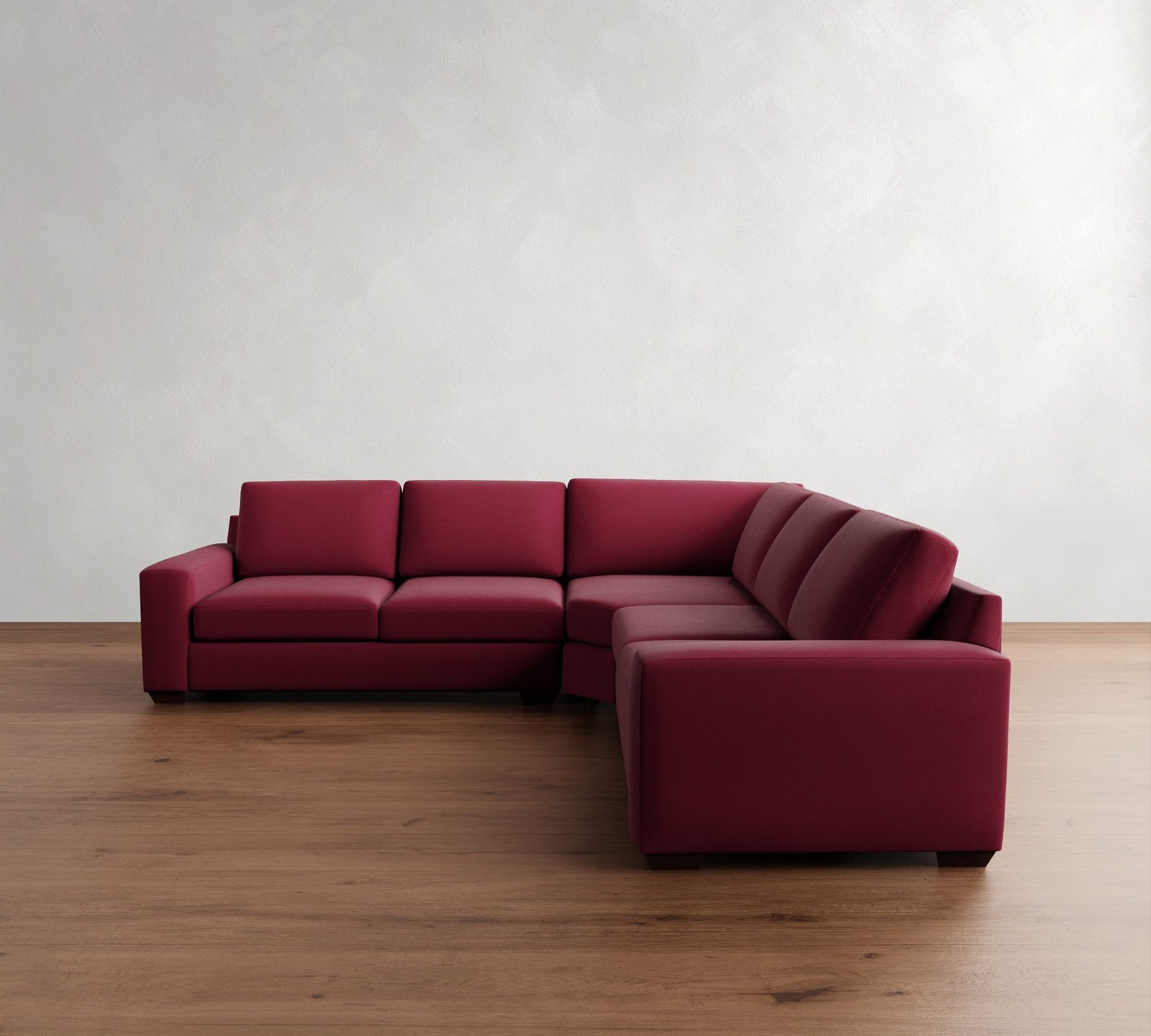 The Big Sur Square Arm Upholstered 3-Piece L-Shaped Wedge Sectional in red features clean lines and is positioned on a polished wooden floor against a textured white wall, forming a cozy corner seating area.