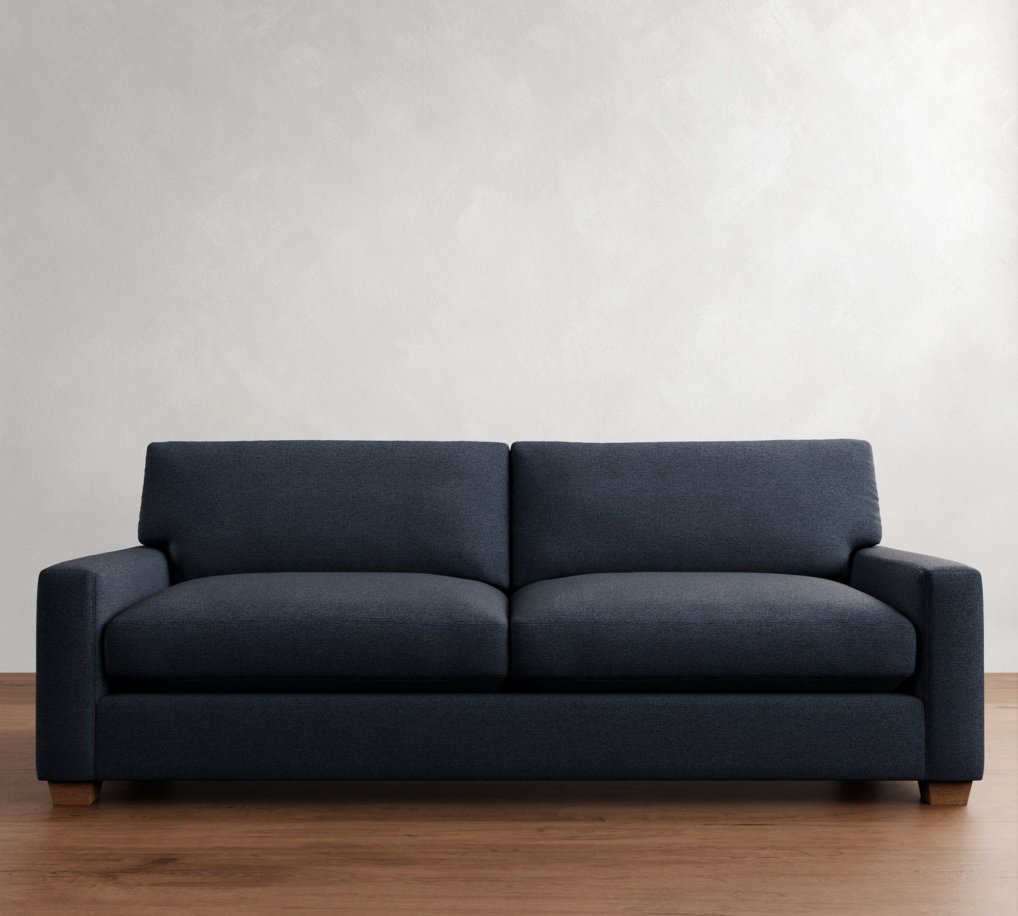 The PB Comfort Modern Square Arm Upholstered Sofa in dark gray, featuring clean lines, is placed against a plain light-colored wall on a wooden floor.