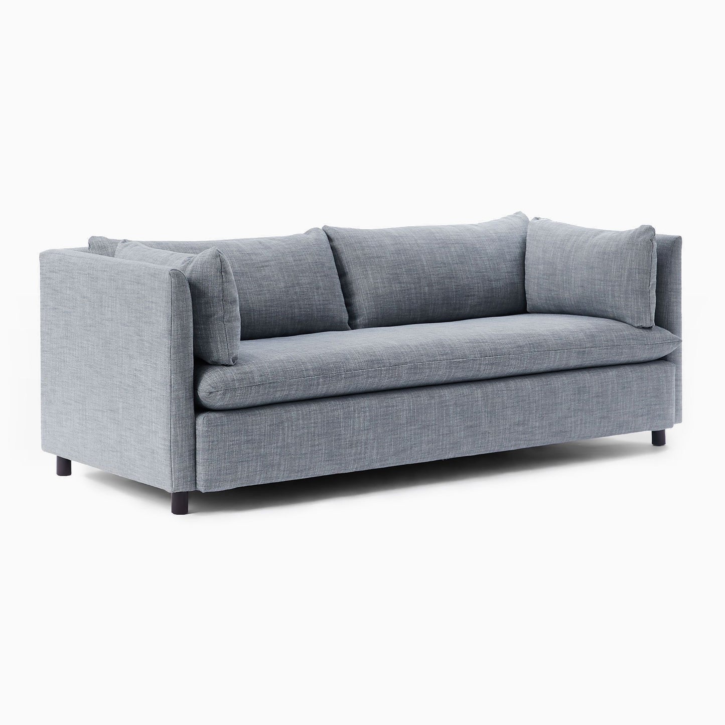 The Shelter Sleeper Sofa features a contemporary design with a light gray fabric and three back cushions, showcasing clean, straight lines. It has a low profile with narrow armrests, supported by dark, short legs, and is displayed on a plain white background.