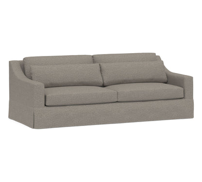 Introducing the York Slope Arm Deep Slipcovered Sofa, a gray two-seater with a modern design. It boasts a smooth fabric texture, gently curved armrests, and two seat cushions. The back is supported by two large, rectangular cushions.