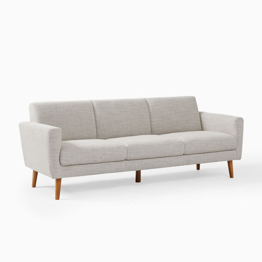 The Oliver Sofa is a modern three-seater with light grey upholstery and wooden legs. It features clean lines and a minimalist aesthetic, making it ideal for contemporary living spaces.