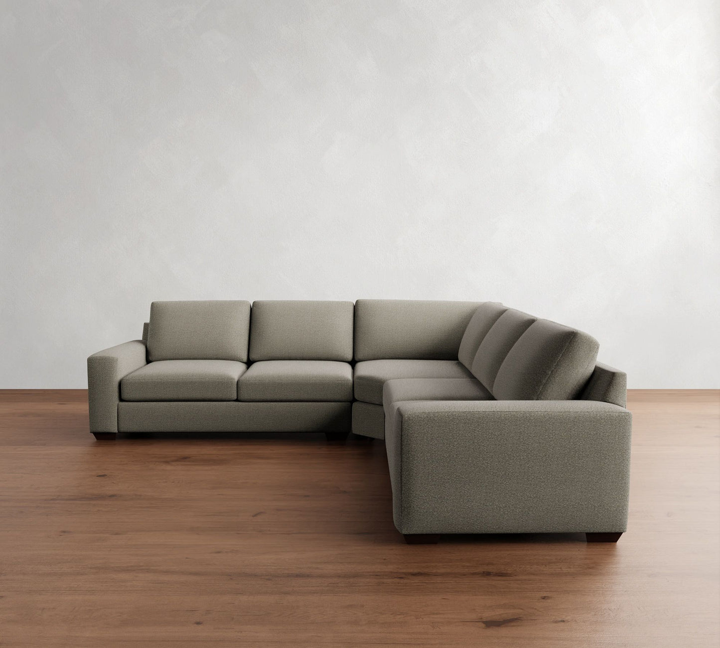 The Big Sur Square Arm Upholstered 3-Piece L-Shaped Wedge Sectional in gray is positioned in the corner of a room with light wooden flooring and a plain off-white wall as the backdrop.