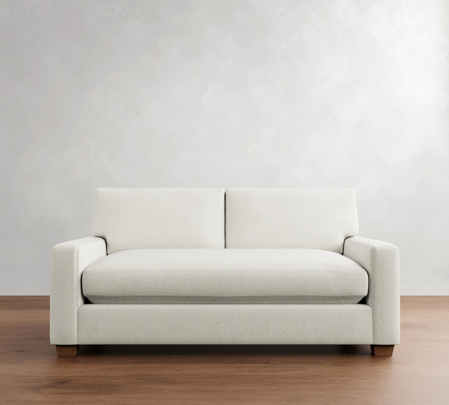 The PB Comfort Modern Square Arm Upholstered Sofa, featuring a sleek minimalist design in white with straight armrests and a single seat cushion, sits against a light gray wall on a wooden floor.